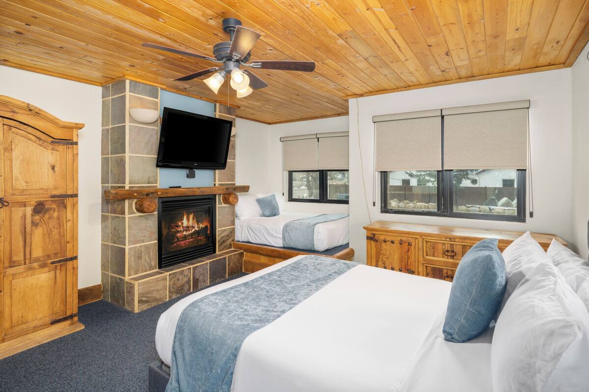 A bedroom with a fireplace, a bed, a television, and a ceiling fan.