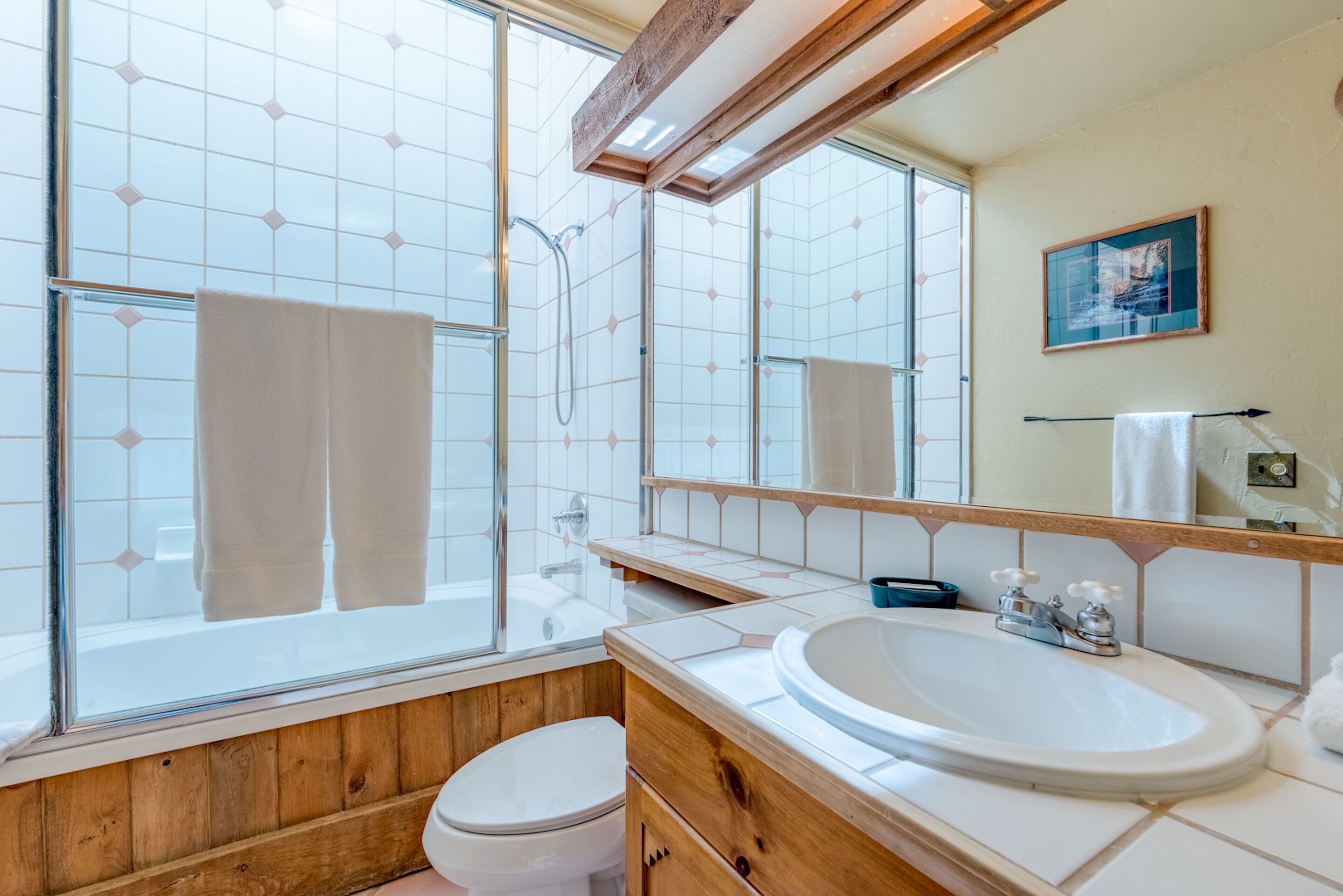 A bathroom with a glass shower enclosure, a wooden vanity, a white sink, and a large mirror.
