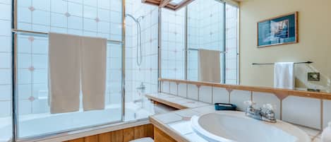 A bathroom with a glass shower enclosure, a wooden vanity, a white sink, and a large mirror.