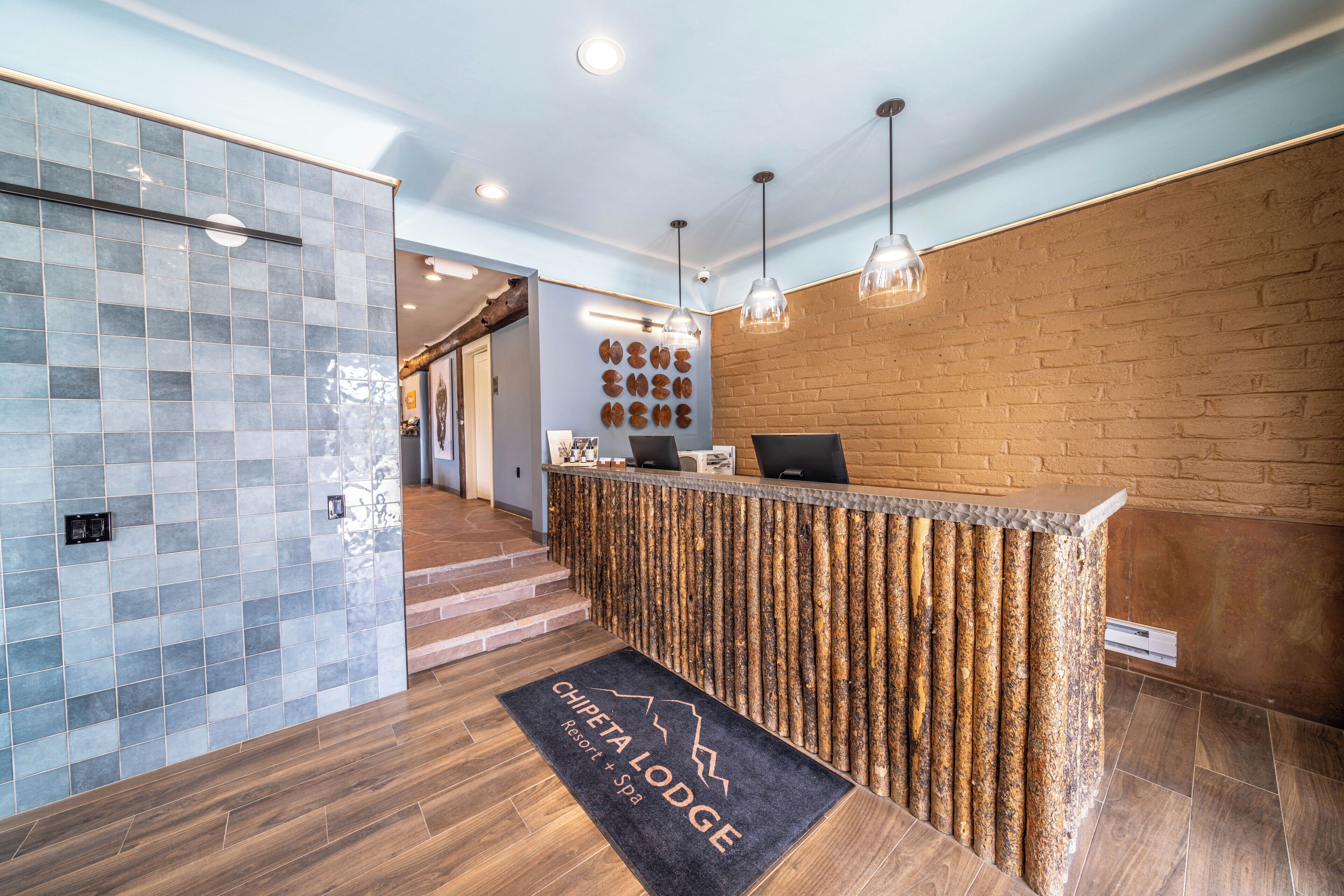 A reception area with a wooden reception desk, a tiled wall, and a doormat that reads "Chipeta Lodge Resort Spa".