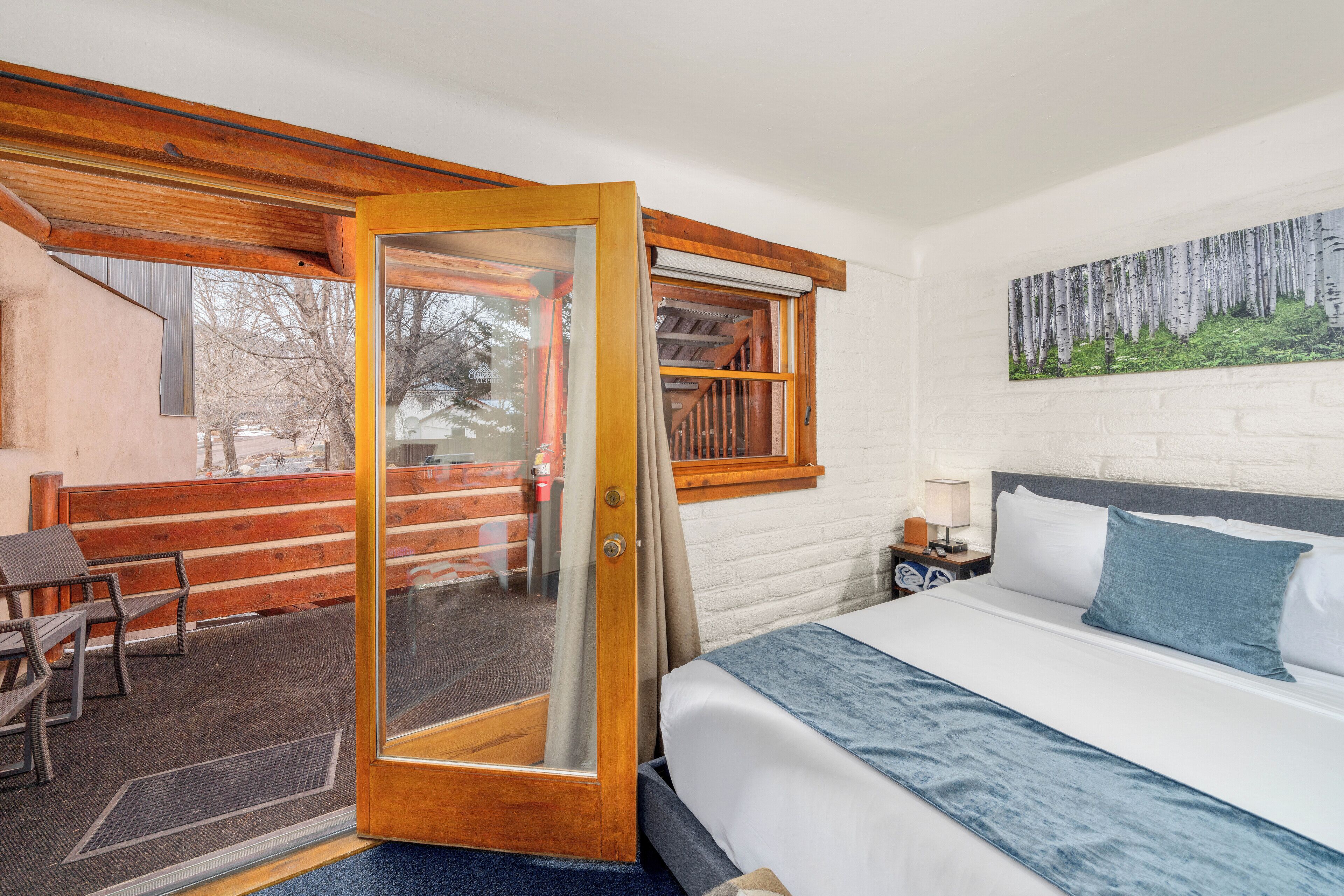 A bedroom with a bed, a window with a view of a wooden deck, and a painting on the wall.