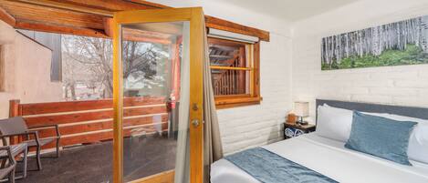 A bedroom with a bed, a window with a view of a wooden deck, and a painting on the wall.