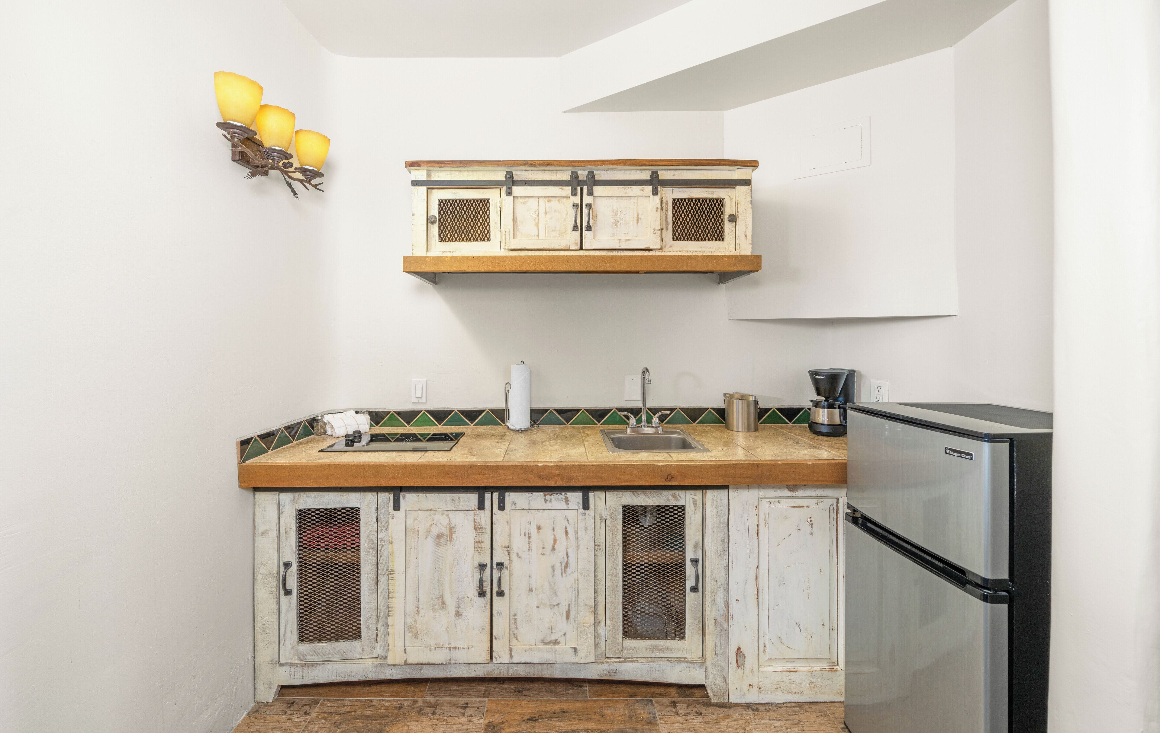 A kitchen with a wooden countertop, a stainless steel refrigerator, and a wall-mounted light fixture.
