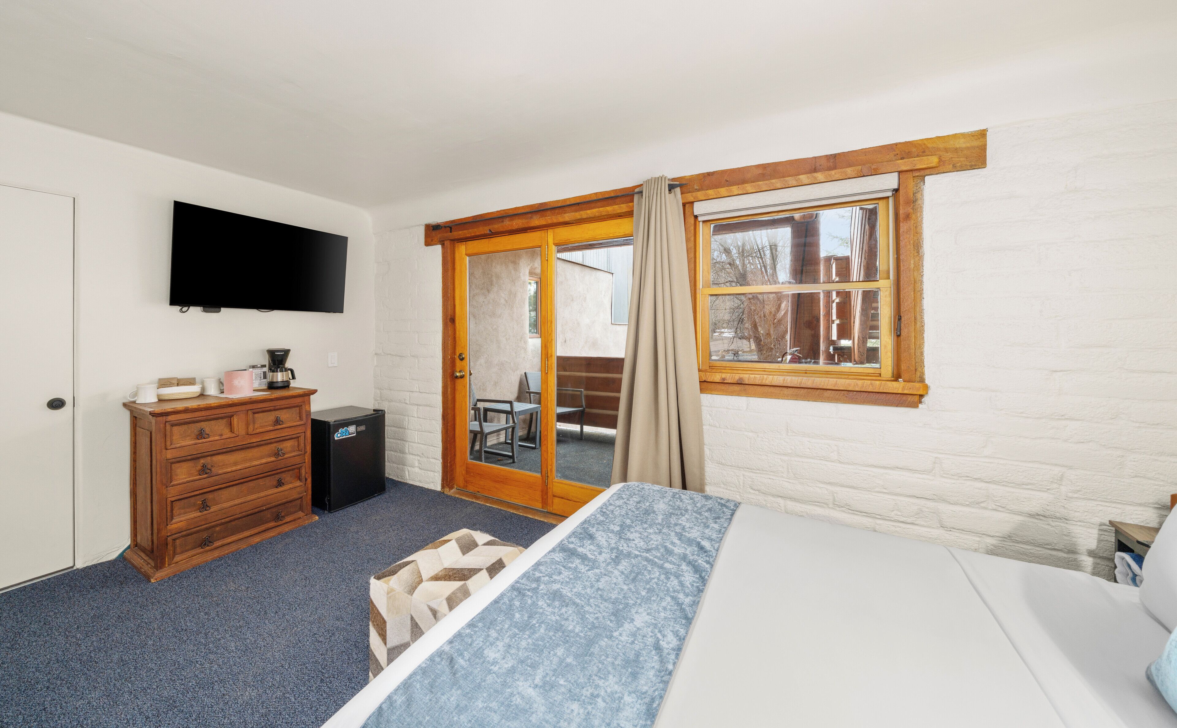 A bedroom with a bed, a dresser, a television, a window, and a door leading to an outdoor area.