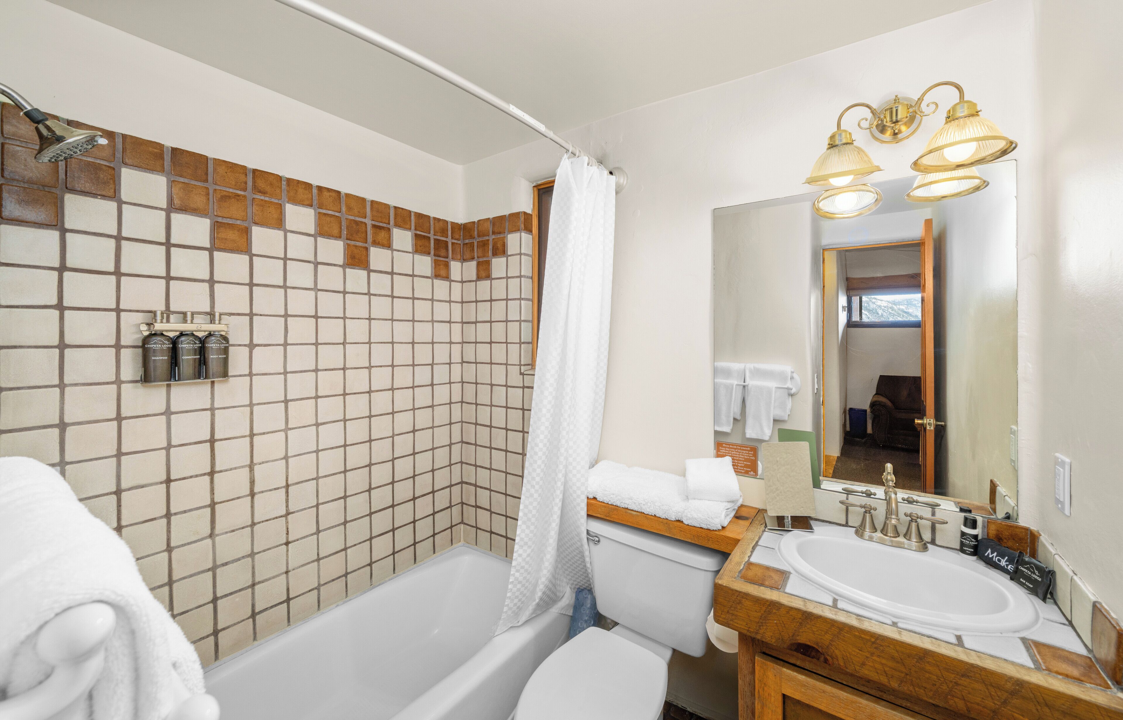 Une salle de bain avec une baignoire, une douche et un lavabo. Il y a un miroir avec des lumières au-dessus, et un porte-serviettes avec des serviettes.