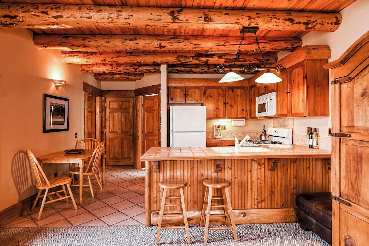 A rustic kitchen with wooden cabinets, a central island with stools, a refrigerator, and a microwave.