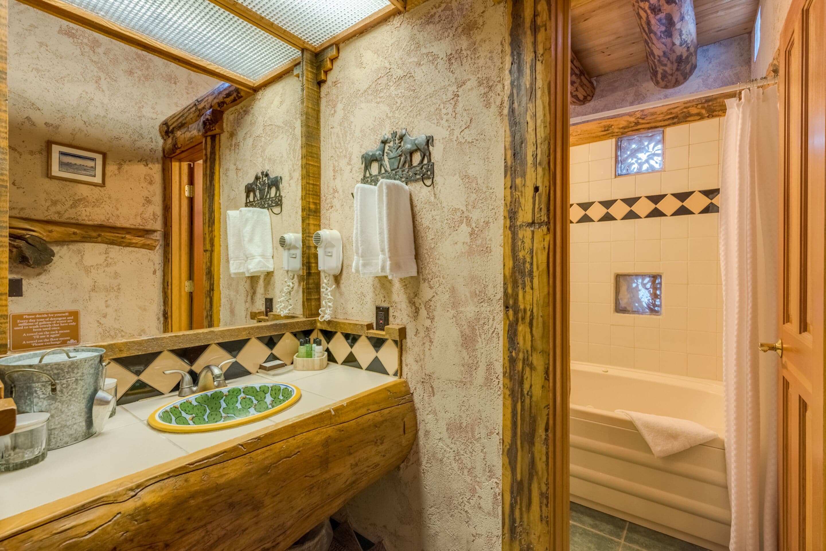 A rustic bathroom with a wooden vanity, a green mosaic sink, and a bathtub with a towel.