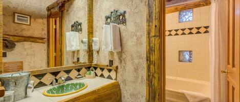 A rustic bathroom with a wooden vanity, a green mosaic sink, and a bathtub with a towel.