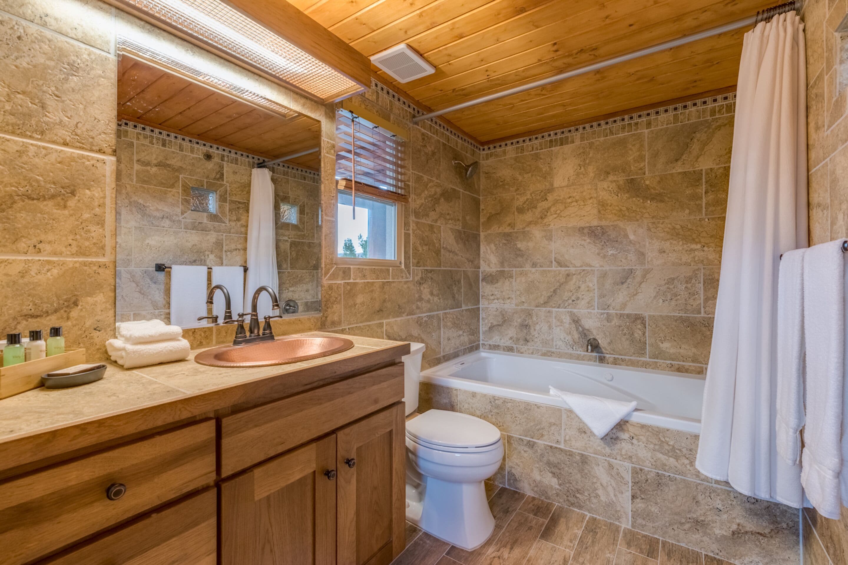 A bathroom with a wooden ceiling, stone walls, a sink, a toilet, and a bathtub.