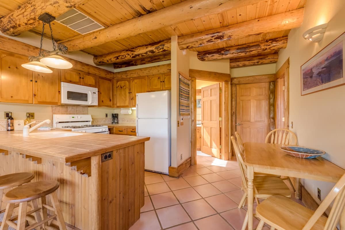 A wooden kitchen with a central island, a microwave, a refrigerator, and a dining table with chairs.