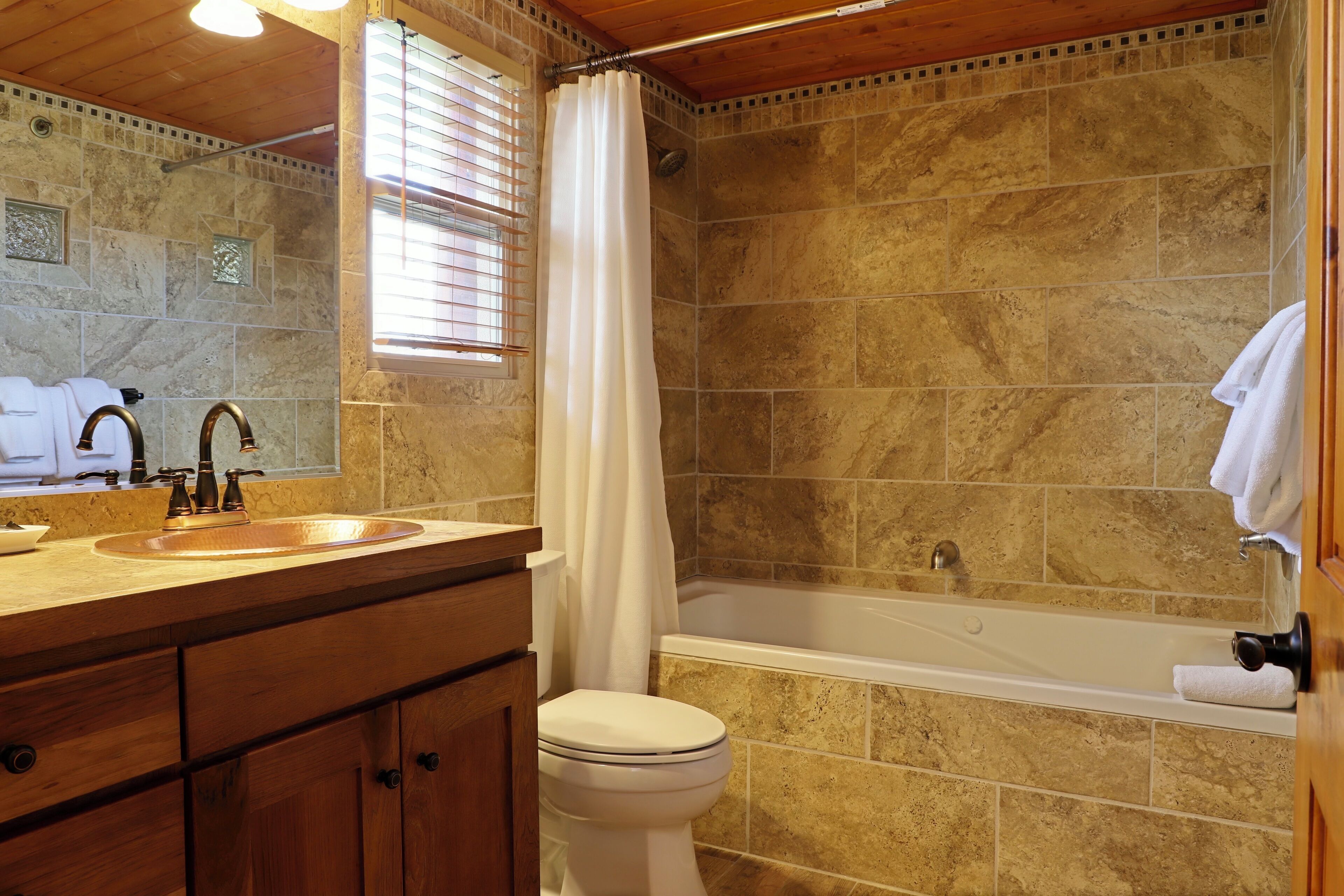 A bathroom with a stone-tiled shower, a white bathtub, and a wooden vanity with a sink.
