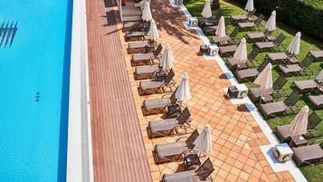 A poolside area with lounge chairs and umbrellas, a tiled deck, and a well-maintained lawn.