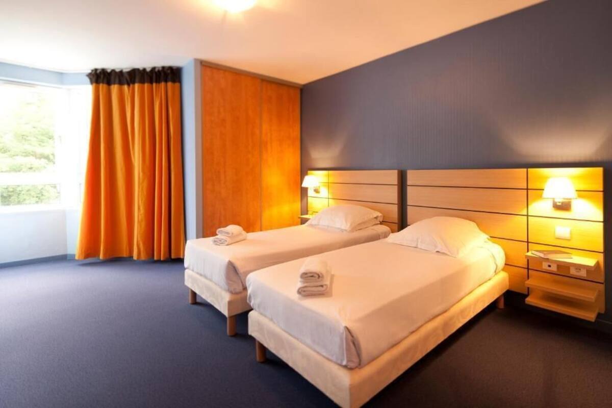 Une chambre d’hôtel avec deux lits, une grande fenêtre avec des rideaux et des lampes de chevet.
