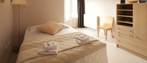 A neatly arranged hotel room with a bed, a chair, a desk, and a wardrobe.