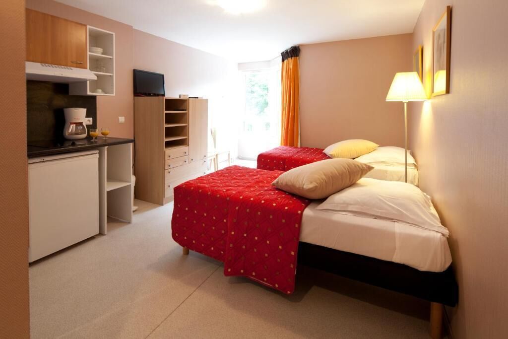 A compact hotel room with a kitchenette, two beds, and a large window.