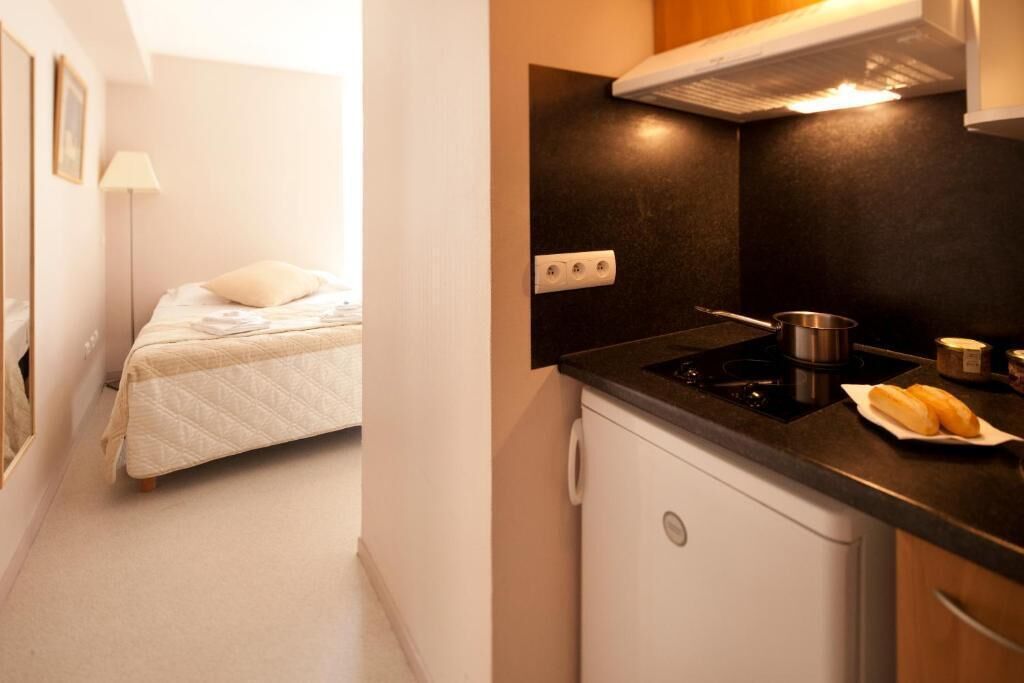 A compact room with a bed, a small kitchenette with a stove, and a white refrigerator.
