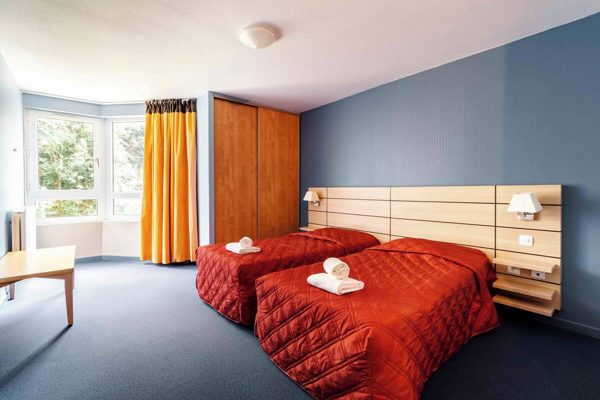 Une chambre d’hôtel avec deux lits, un bureau, une armoire et une fenêtre avec des rideaux.