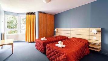 Ein Hotelzimmer mit zwei Betten, einem Schreibtisch, einem Kleiderschrank und einem Vorhangfenster.