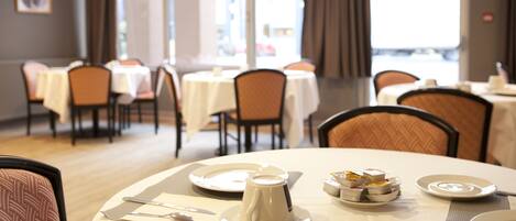 A dining area with tables set for two, featuring white tablecloths, plates, and cutlery.