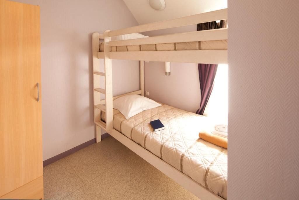 Habitació amb lliteres de fusta, un matalàs blanc i un llibre damunt el llit.
