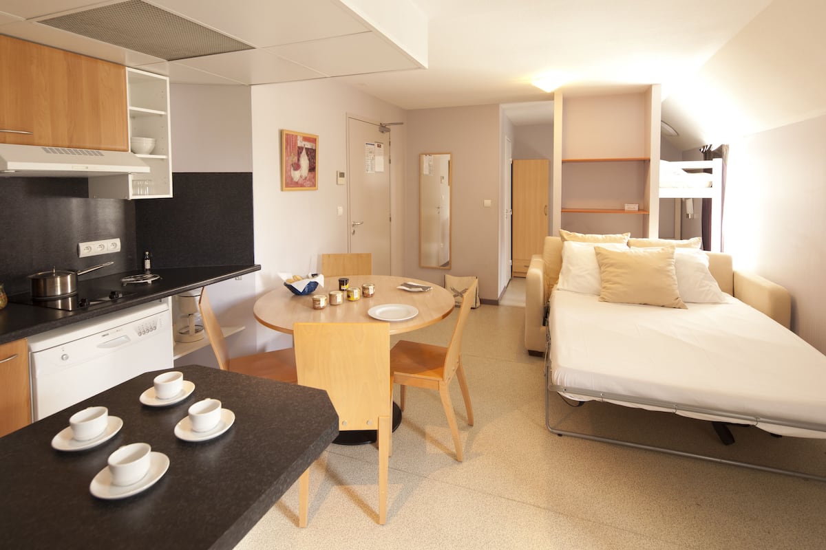 Une chambre d’hôtel compacte comprenant un coin cuisine, un espace repas, un lit et un dressing.