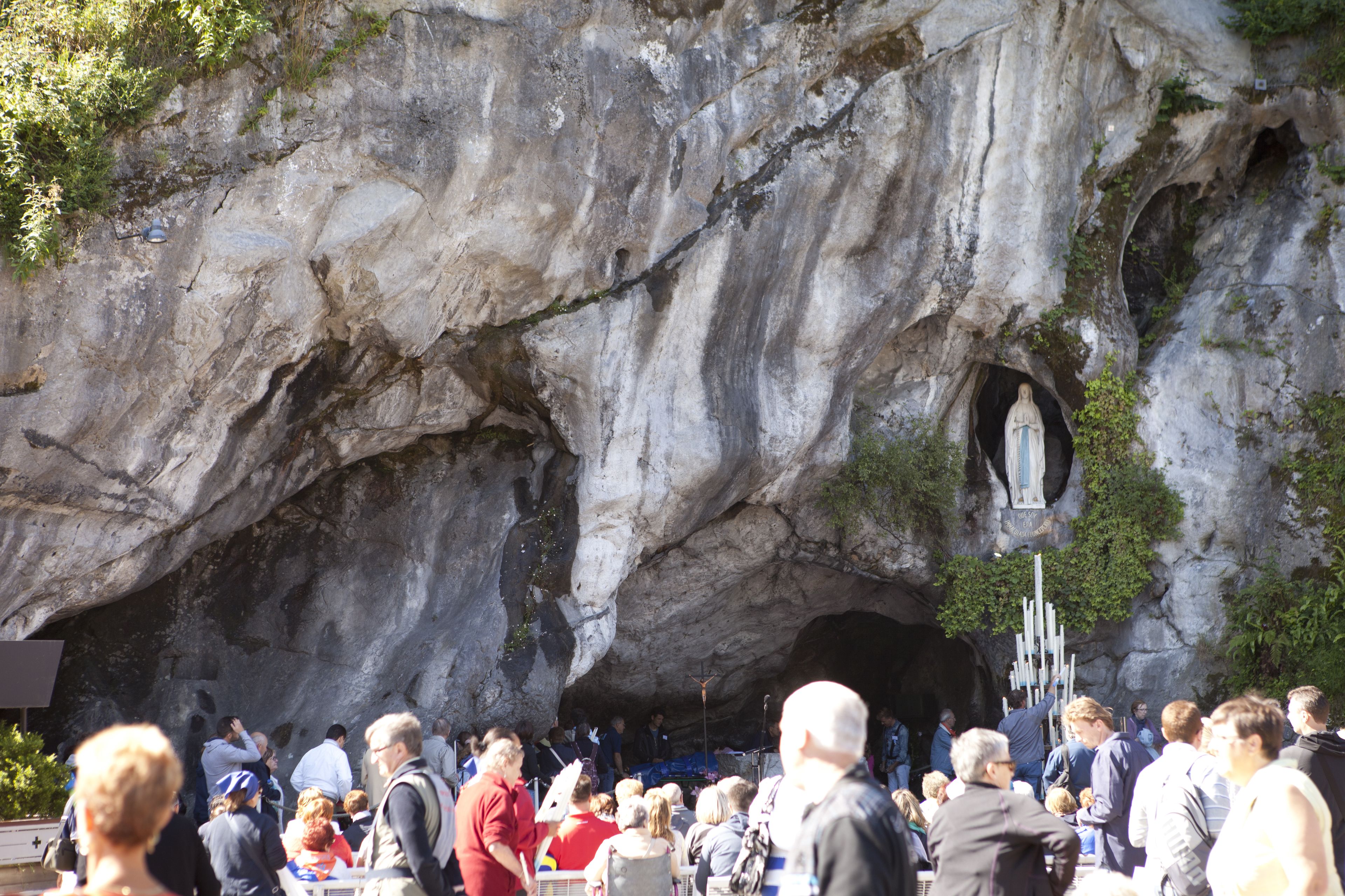 A large cave-like structure with a statue inside, surrounded by a crowd of people.