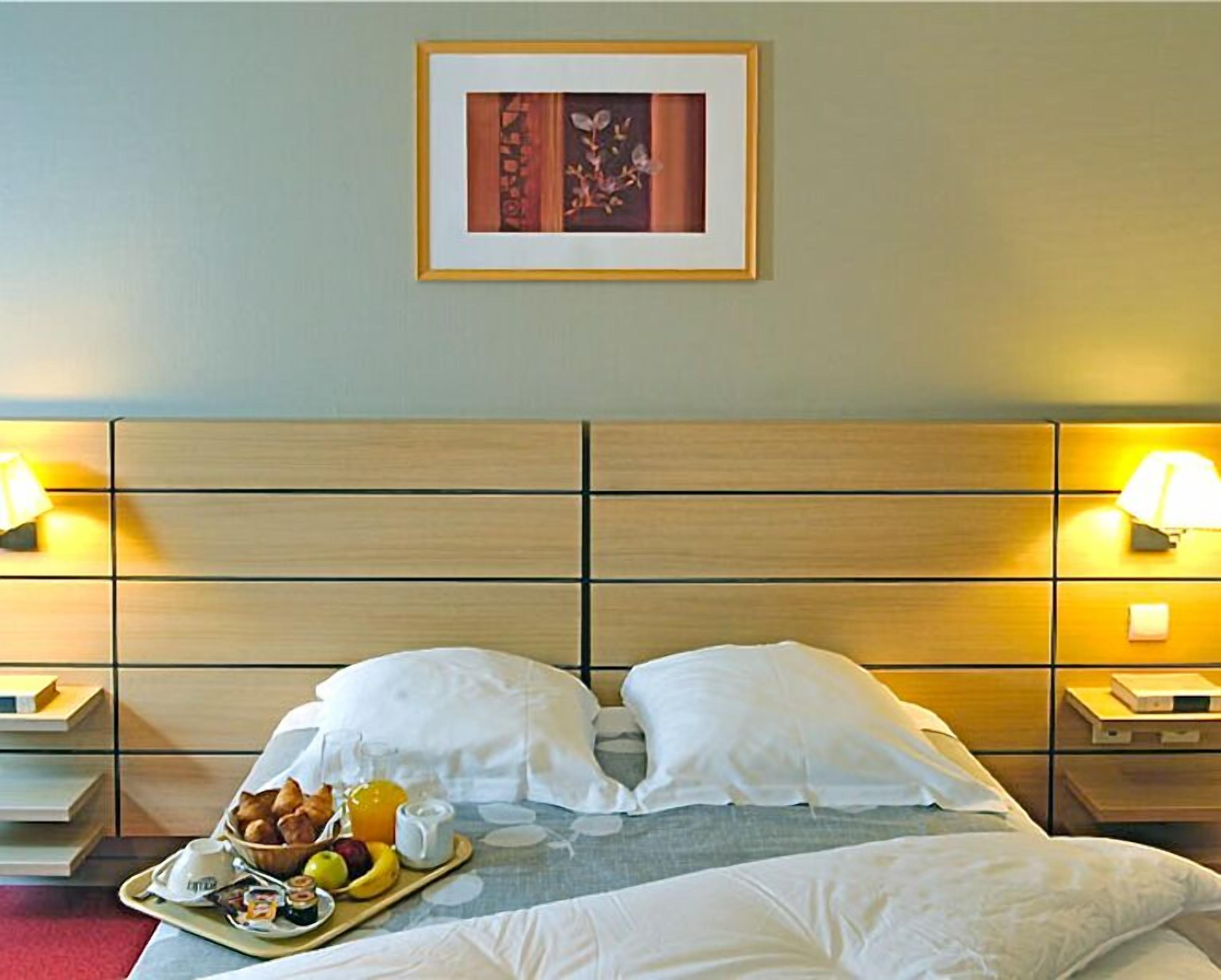 Ein Hotelzimmer mit einem Bett, zwei Nachttischlampen, einem gerahmten Bild an der Wand und einem Tablett mit Frühstücksgebäck.