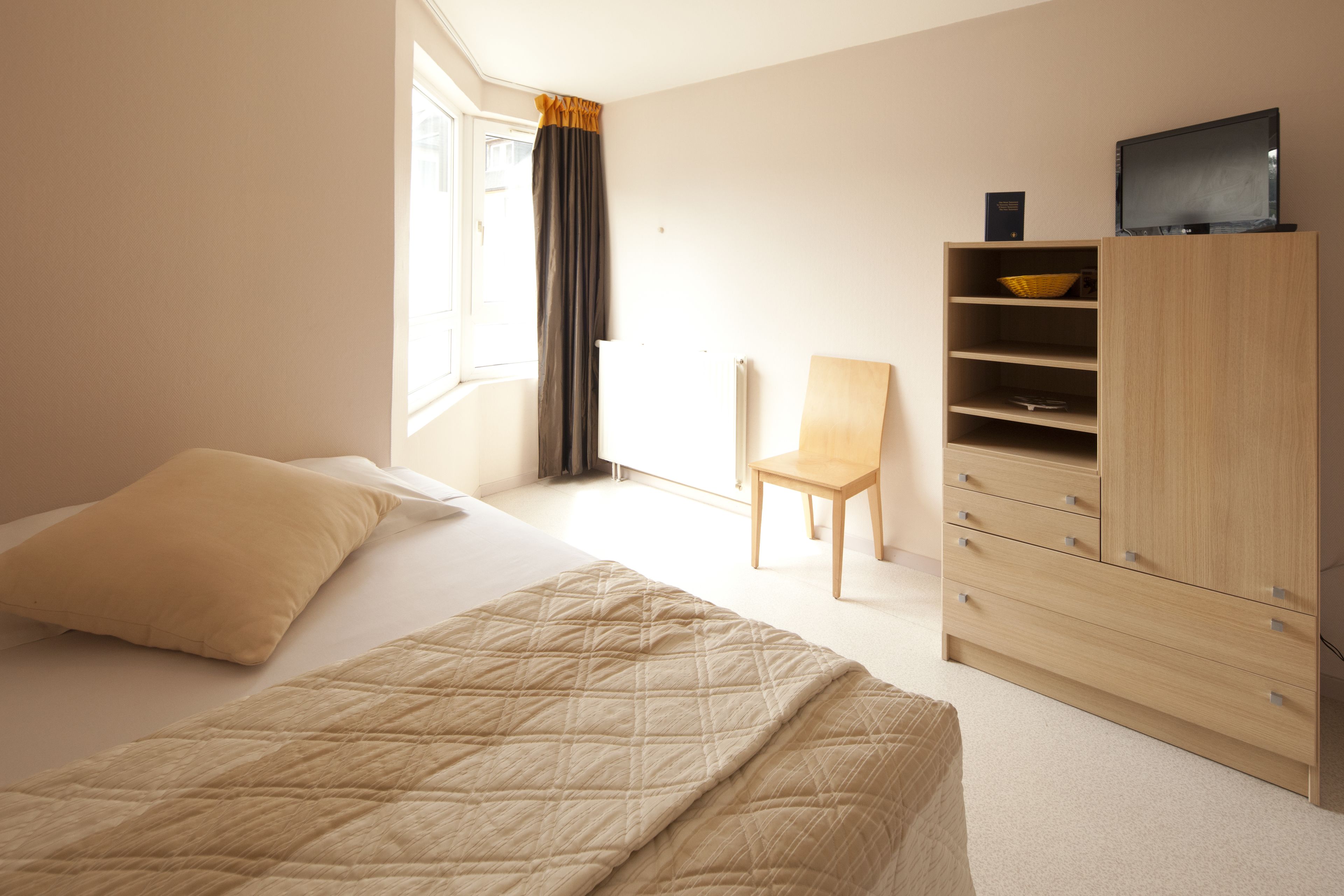 A bedroom with a bed, a chair, a wardrobe, and a television.