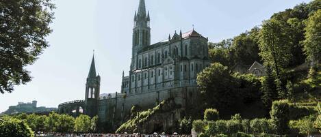 A historic cathedral with a prominent tower and a large, ornate facade, situated beside a river with a bridge in the background.