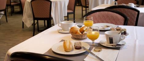 Desayuno con croissants, zumo de naranja y bollería sobre una mesa.