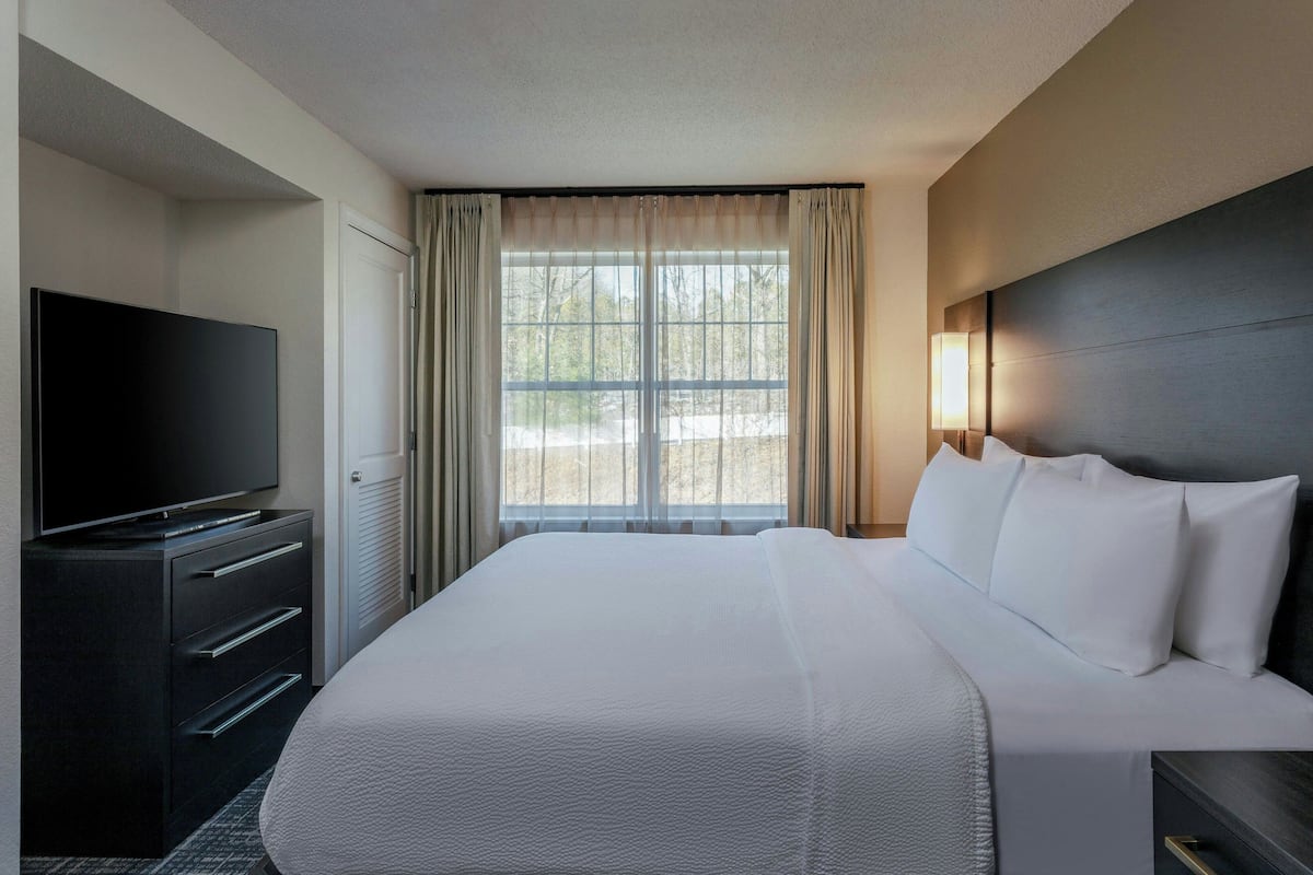 A hotel room with a large bed, a flat-screen TV, a dresser, and a window with curtains.