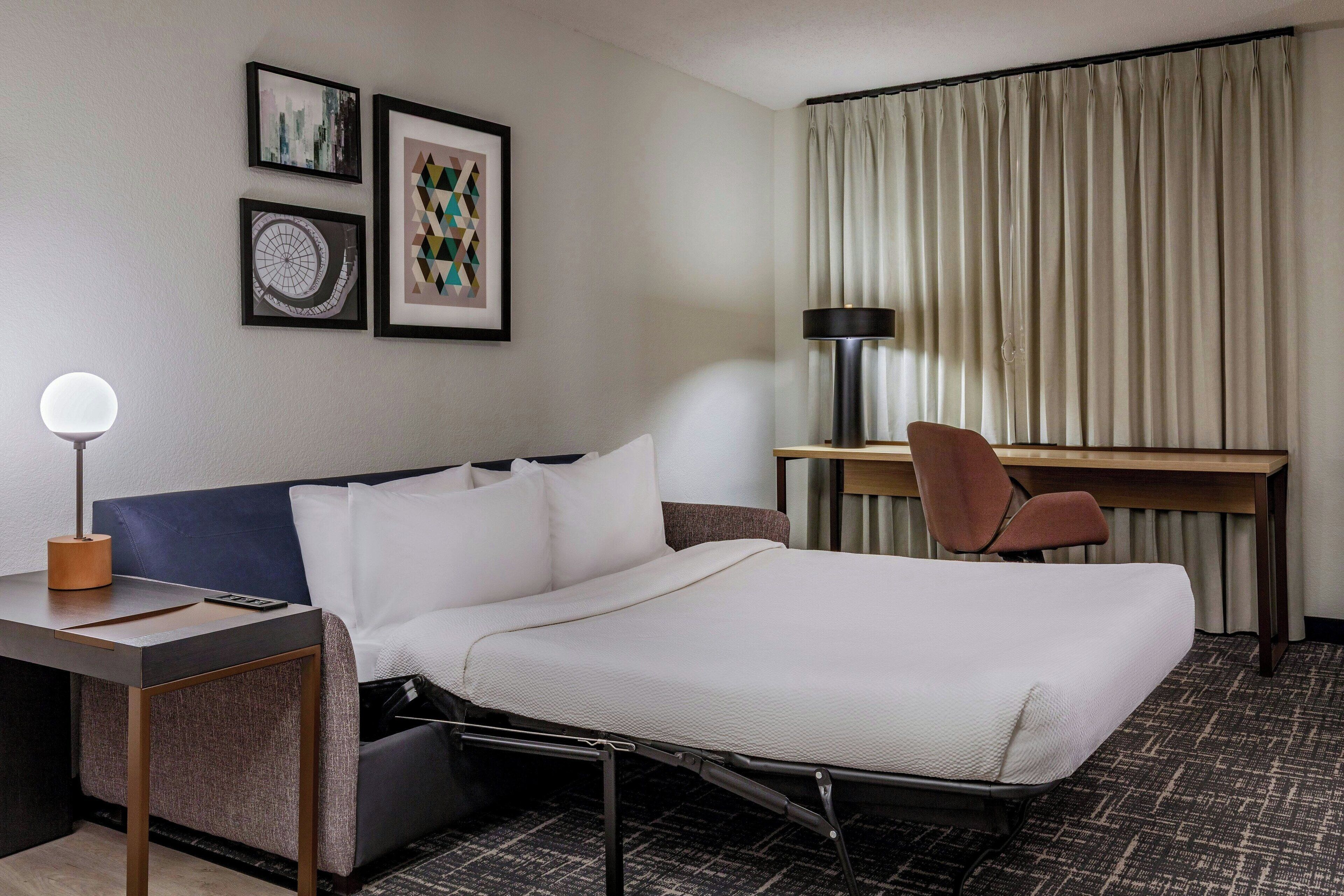 Ein Hotelzimmer mit Bett, Schreibtisch, Stuhl und Lampe. An den Wänden befinden sich gerahmte Bilder.