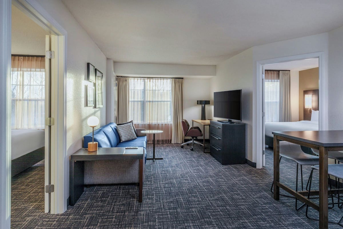 A hotel room with a bed, a sofa, a desk, a TV, and a dining area.