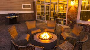 A circular fire pit surrounded by wicker chairs in an outdoor seating area with a brick wall and large windows in the background. - Residence Inn by Marriott Worcester (Worcester)