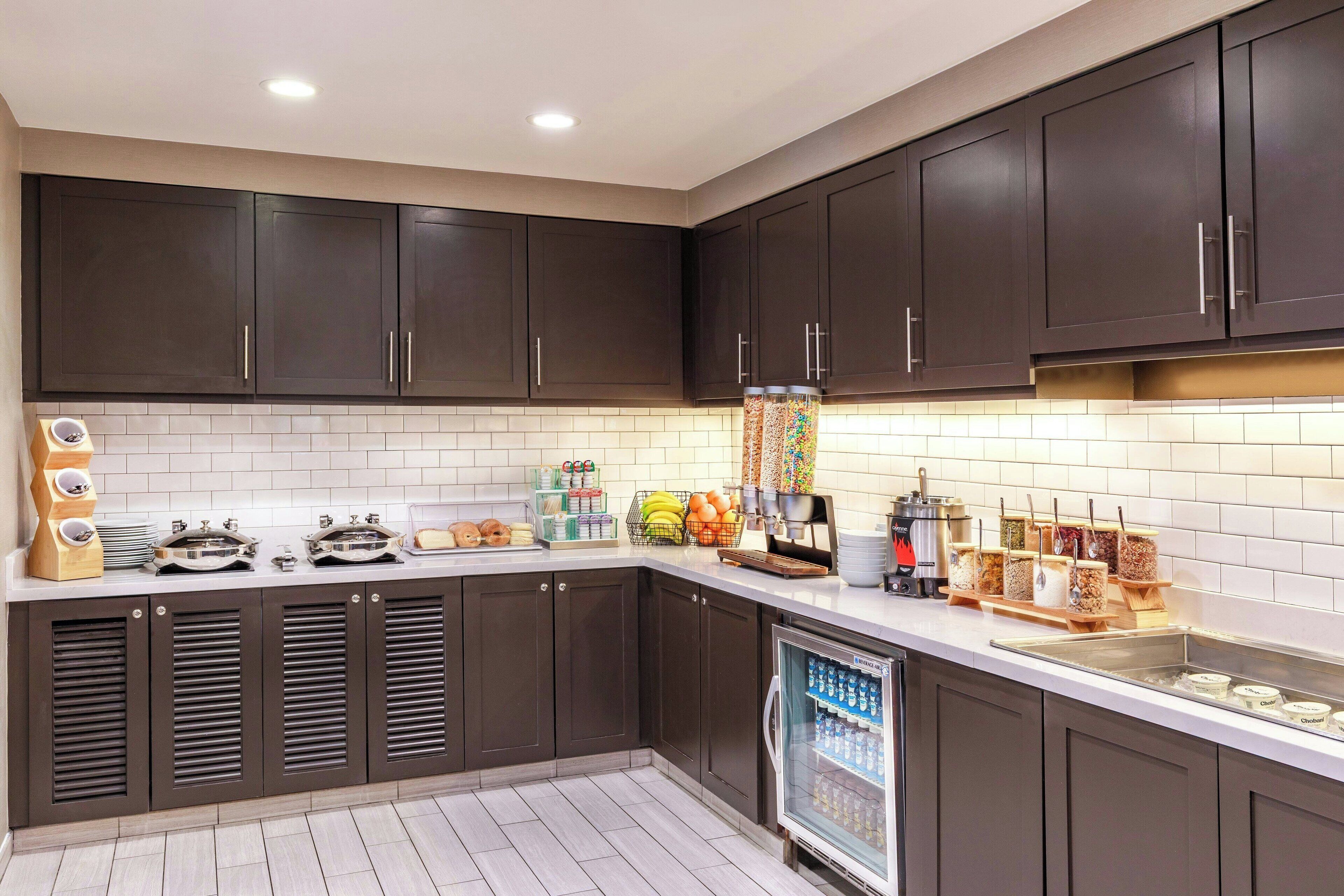 Uma cozinha moderna com armários marrom escuro, painel de azulejos branco e uma geladeira de aço inoxidável.
