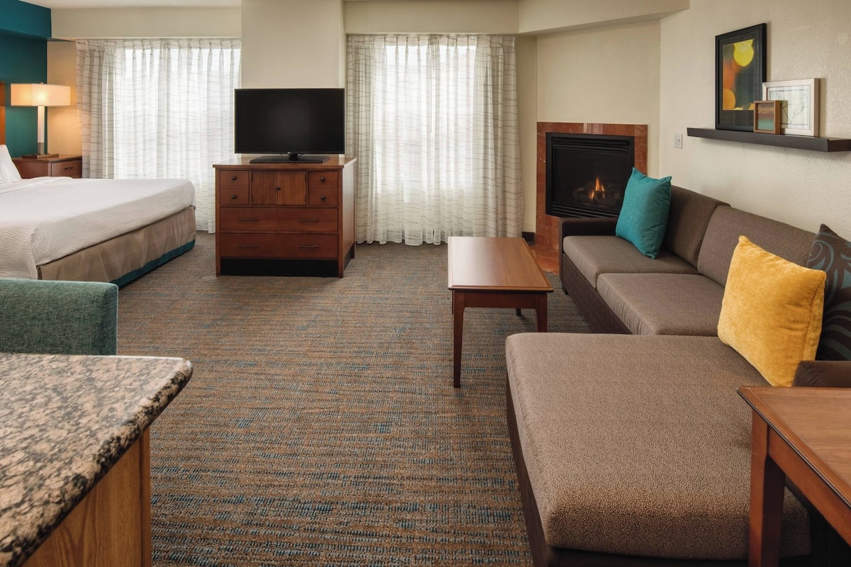 Una habitación de hotel con cama, sofá, televisión, chimenea y escritorio.