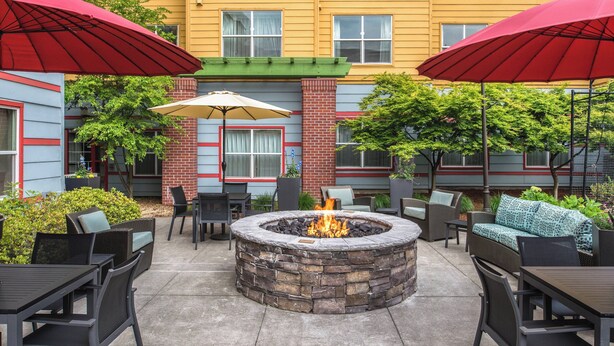 Une terrasse extérieure avec un foyer en pierre, des meubles en métal noir et des parasols rouges.