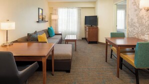 Une chambre d’hôtel avec un canapé, une petite table, un téléviseur et un bureau avec des chaises.