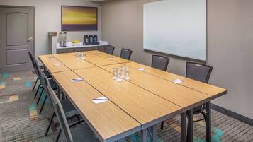 A conference room with a long table, chairs, a projector screen, and a coffee station.