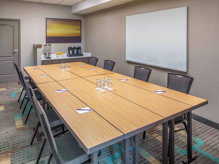A conference room with a long table, chairs, a projector screen, and a coffee station.
