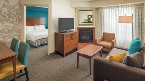 Une chambre d’hôtel comprenant un lit, un téléviseur posé sur un meuble en bois, une cheminée, un canapé, une table basse et une table à manger avec des chaises.