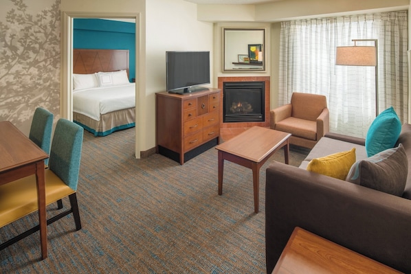 A hotel room with a bed, a TV on a wooden cabinet, a fireplace, a sofa, a coffee table, and a dining table with chairs.