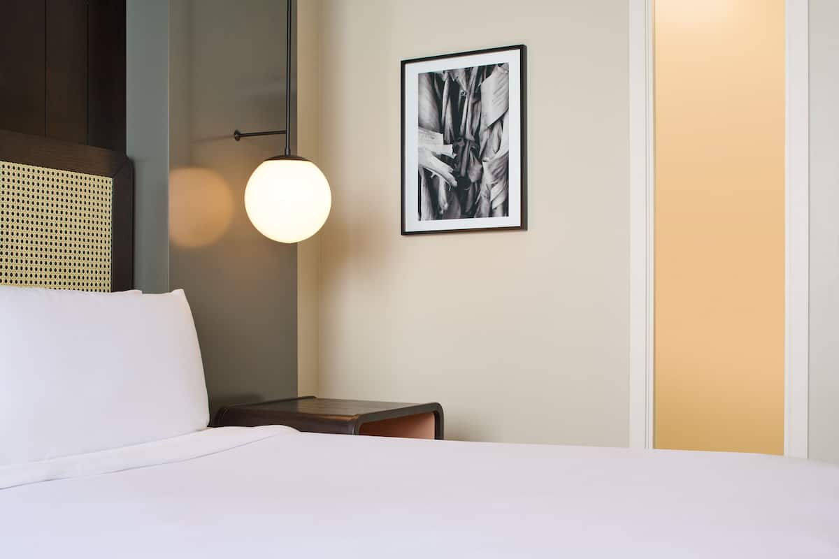 Une chambre d’hôtel avec un lit, une table de chevet, une lampe fixée au mur et un tableau encadré.
