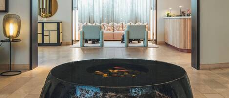 Un intérieur moderne avec un élément décoratif central composé d’un jeu d’eau, un ensemble de canapés et un coin repas.