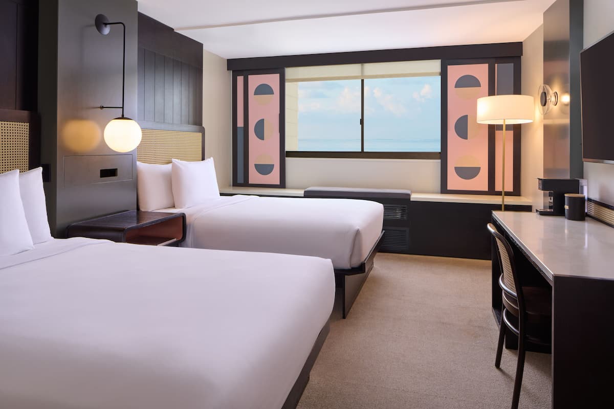 Une chambre d’hôtel avec deux lits, un bureau, une chaise, une lampe et une vue sur la mer.