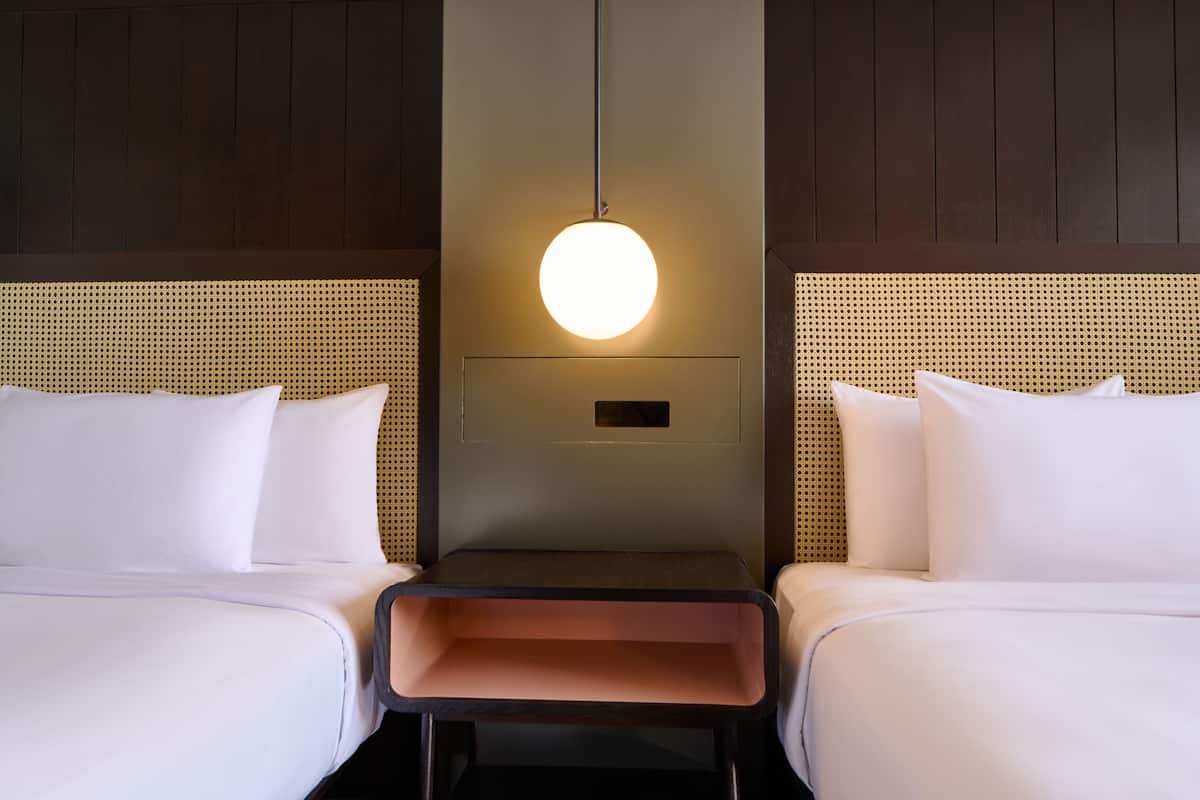 Une chambre d’hôtel avec deux lits, une table de chevet centrale et un luminaire fixé au mur.