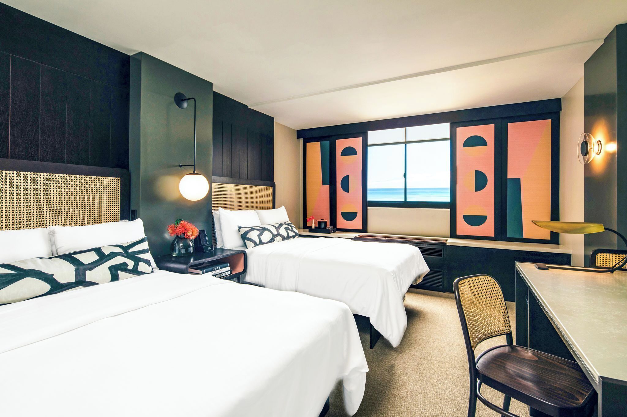 Une chambre d’hôtel avec deux lits, un bureau, une chaise, une lampe et une grande fenêtre donnant sur un beau paysage.