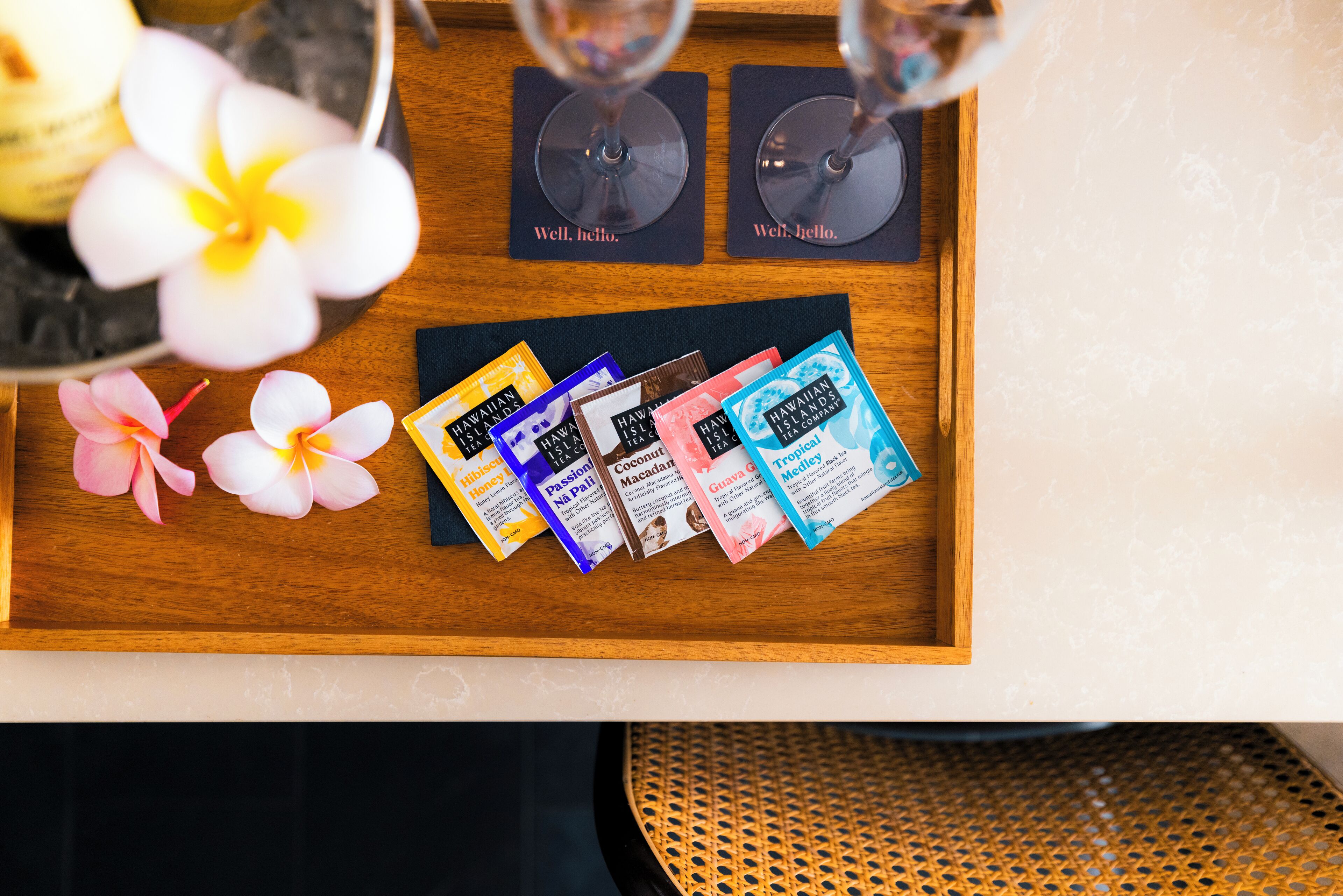 A wooden tray with a selection of Hawaiian-themed gift cards, two wine glasses, and a few flowers.
