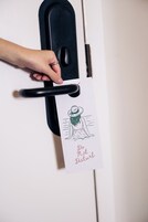 Une main tenant la poignée d’une porte, avec un panneau indiquant « Ne pas déranger » et un dessin d’une personne portant un chapeau.