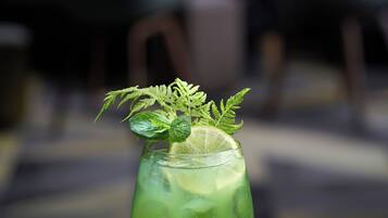 A glass of green drink with mint leaves and a lime slice, placed on a stone surface with two decorative stones.